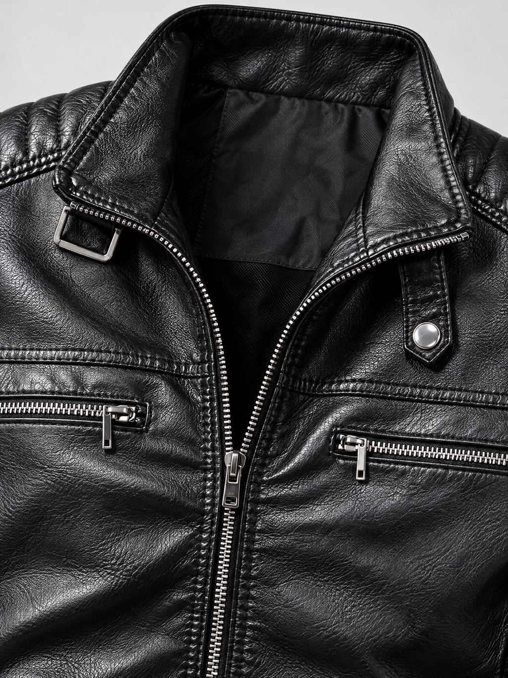 Close-up of a Black Biker Leather Jacket with a notched collar, buckle detail, snap tab, and silver zippered chest pockets.