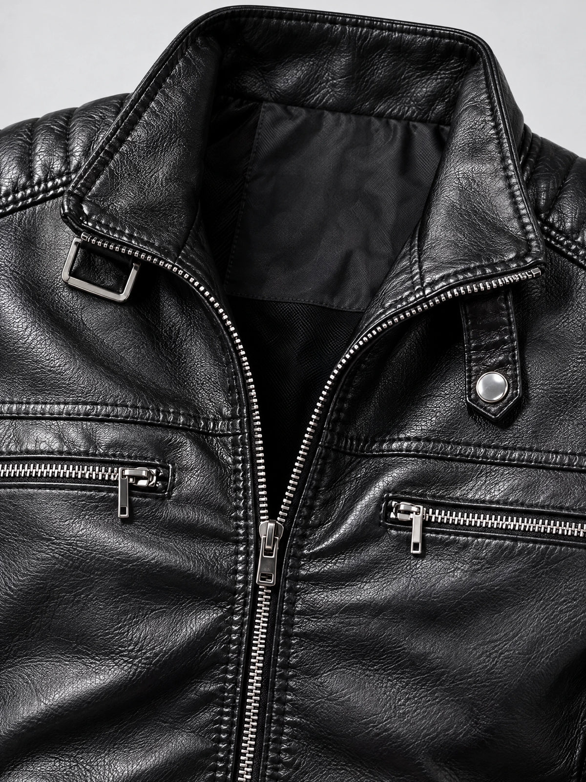 Close-up of a Black Biker Leather Jacket with a notched collar, buckle detail, snap tab, and silver zippered chest pockets.