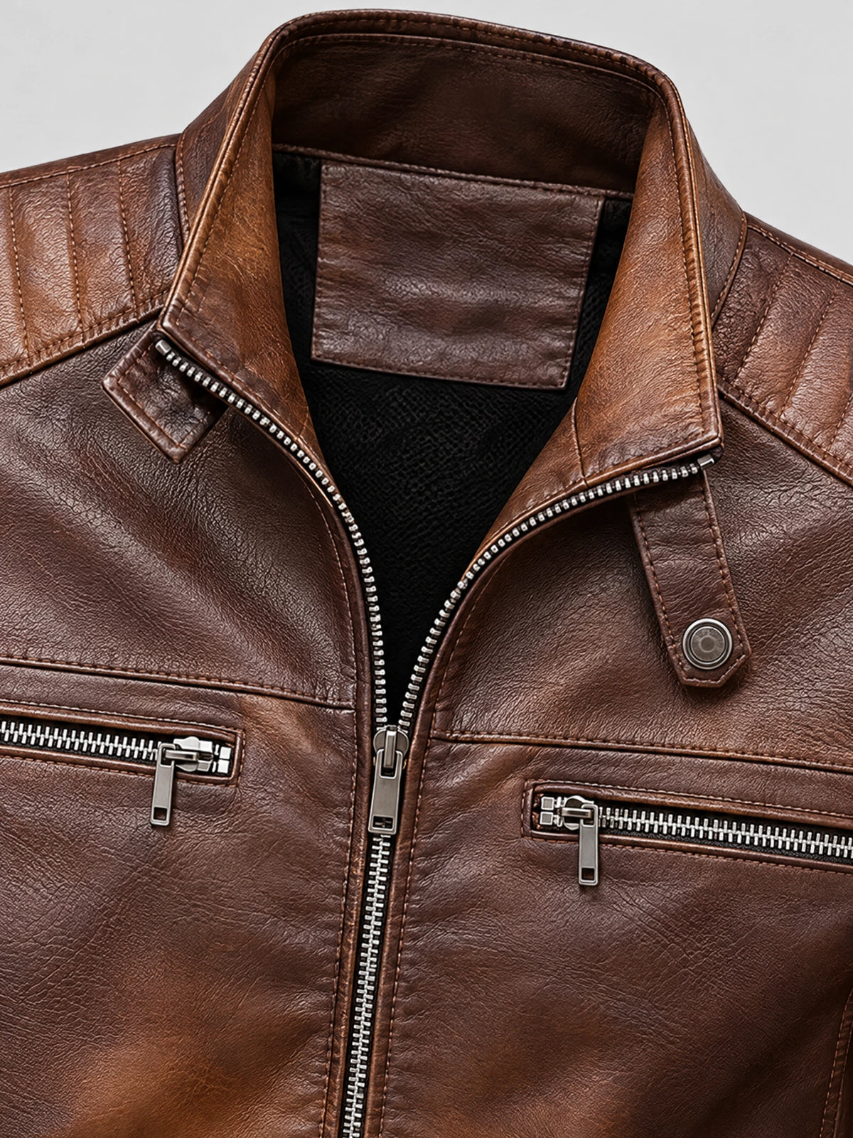 Brown biker leather jacket close-up showing the textured PU leather lapel, front zipper, and zippered chest pockets.