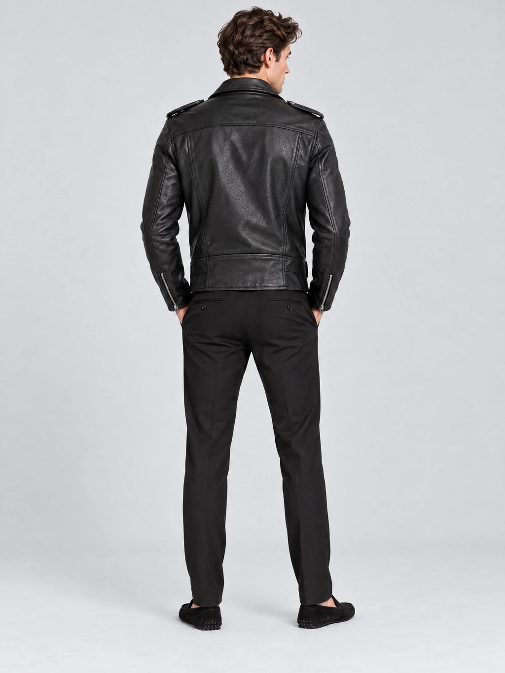 Rear studio view of a model wearing a Black Biker Leather Jacket with shoulder epaulets, back seams, and zippered cuffs.