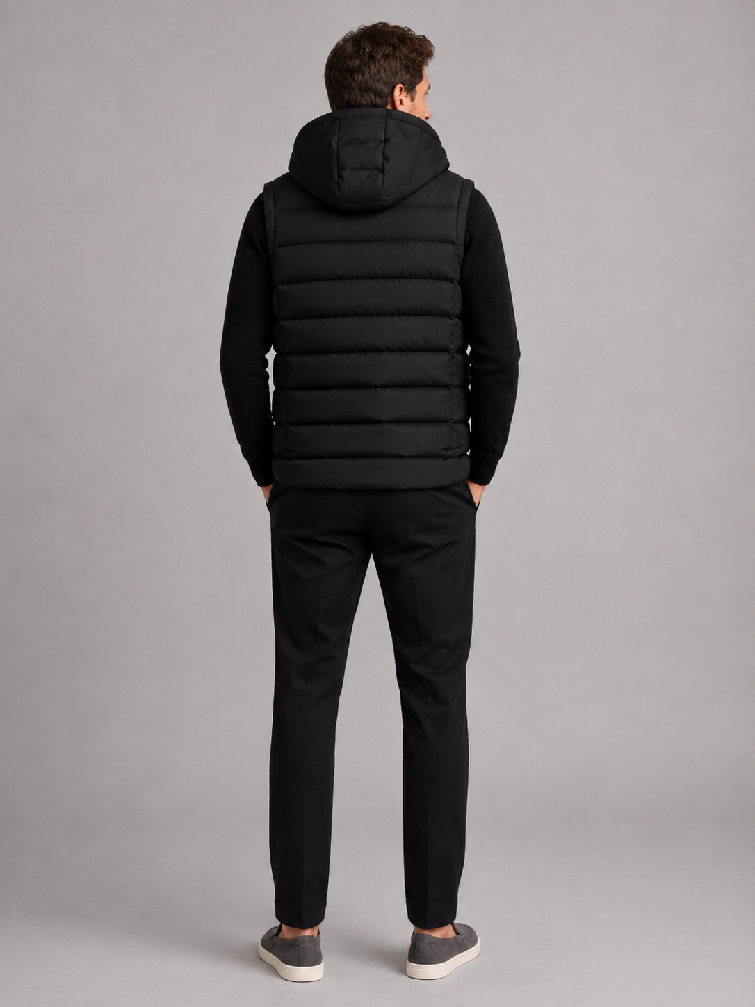 Back view of a man wearing a black hooded puffer vest showing the attached hood, padded construction, sleeveless cut, and comfortable fit