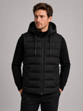 Front view of a man wearing a black hooded puffer vest with cotton padding, thick insulation, sleeveless design, and full zip front