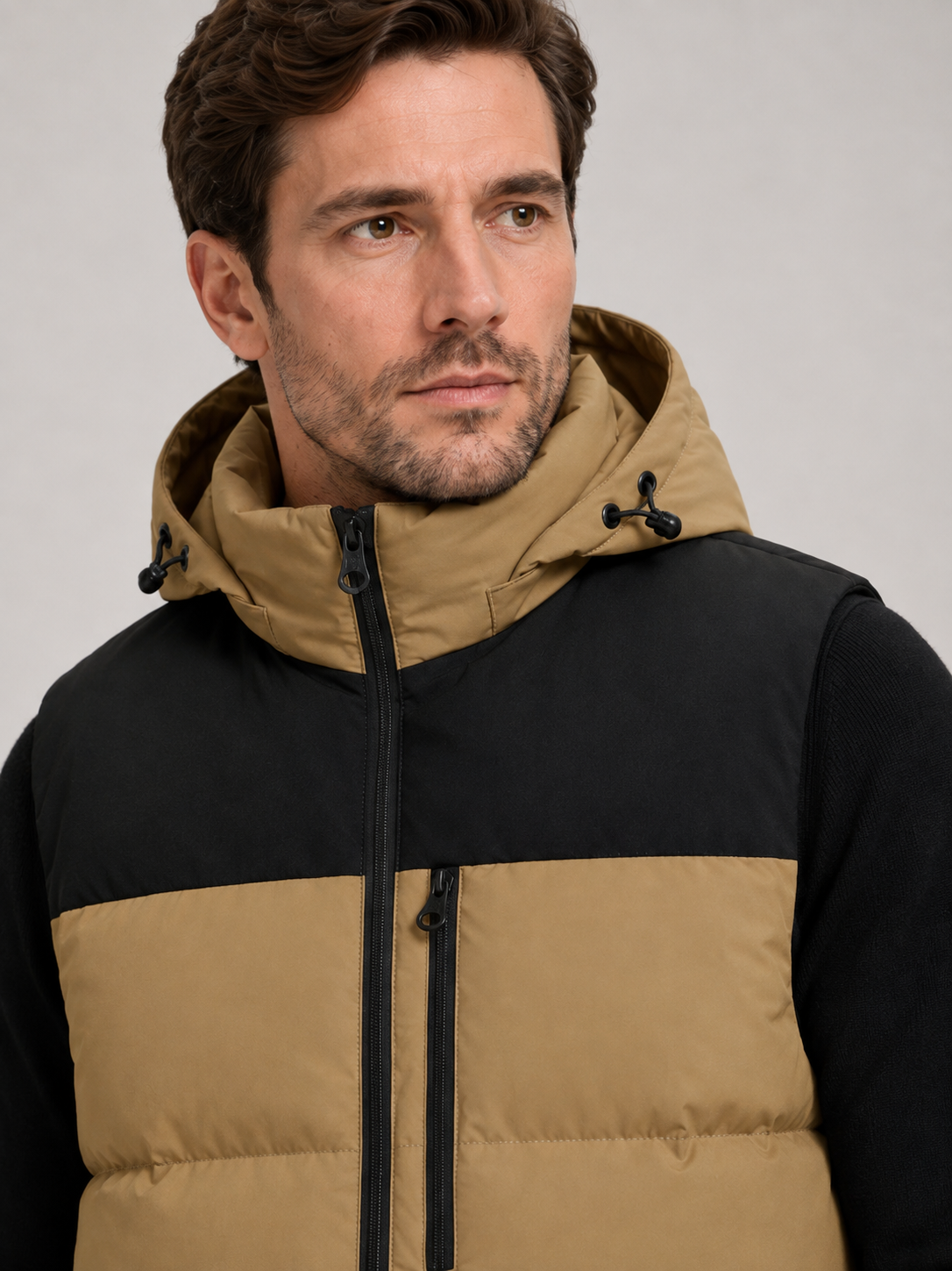Close-up of a brown hooded puffer vest showing the windproof fabric, thick insulation, zipper closure, hood, pockets, armholes, and stitching details