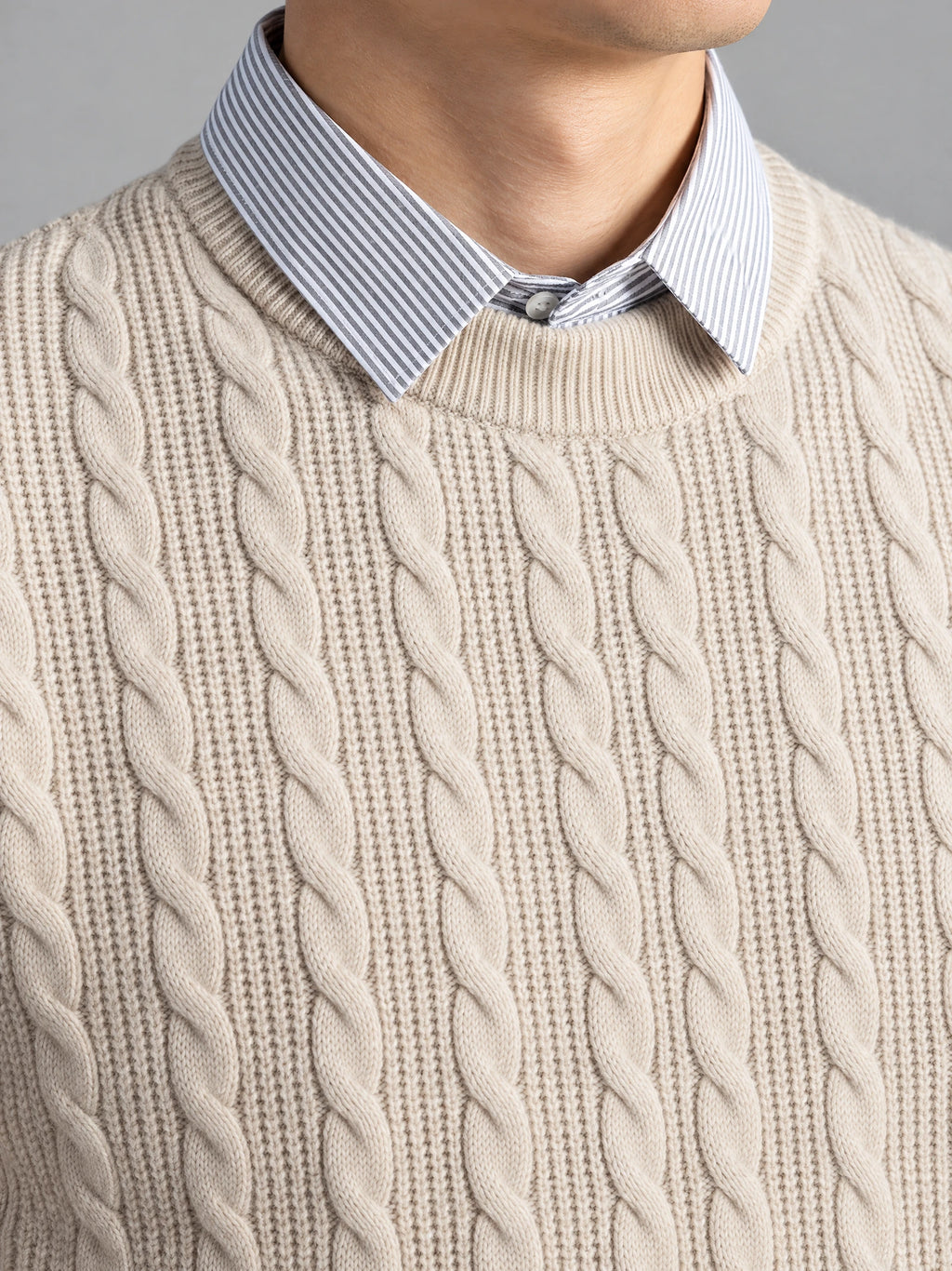 Close-up of a Beige business casual knitted pullover sweater with cable-knit texture, ribbed crew neckline, and faux striped shirt collar.