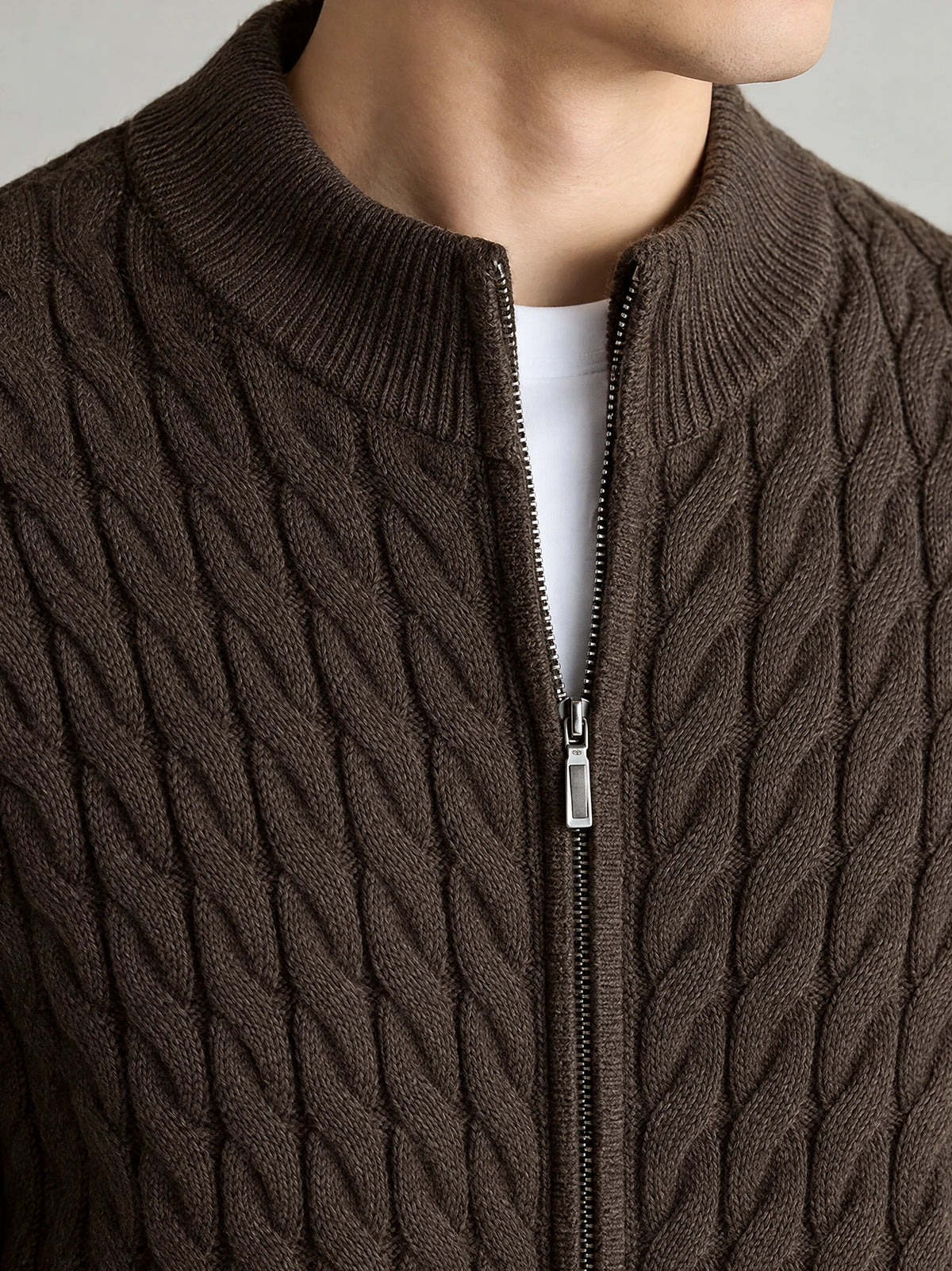 Close-up of a Brown cable knit full zip sweater with a ribbed round neckline and metal zipper.