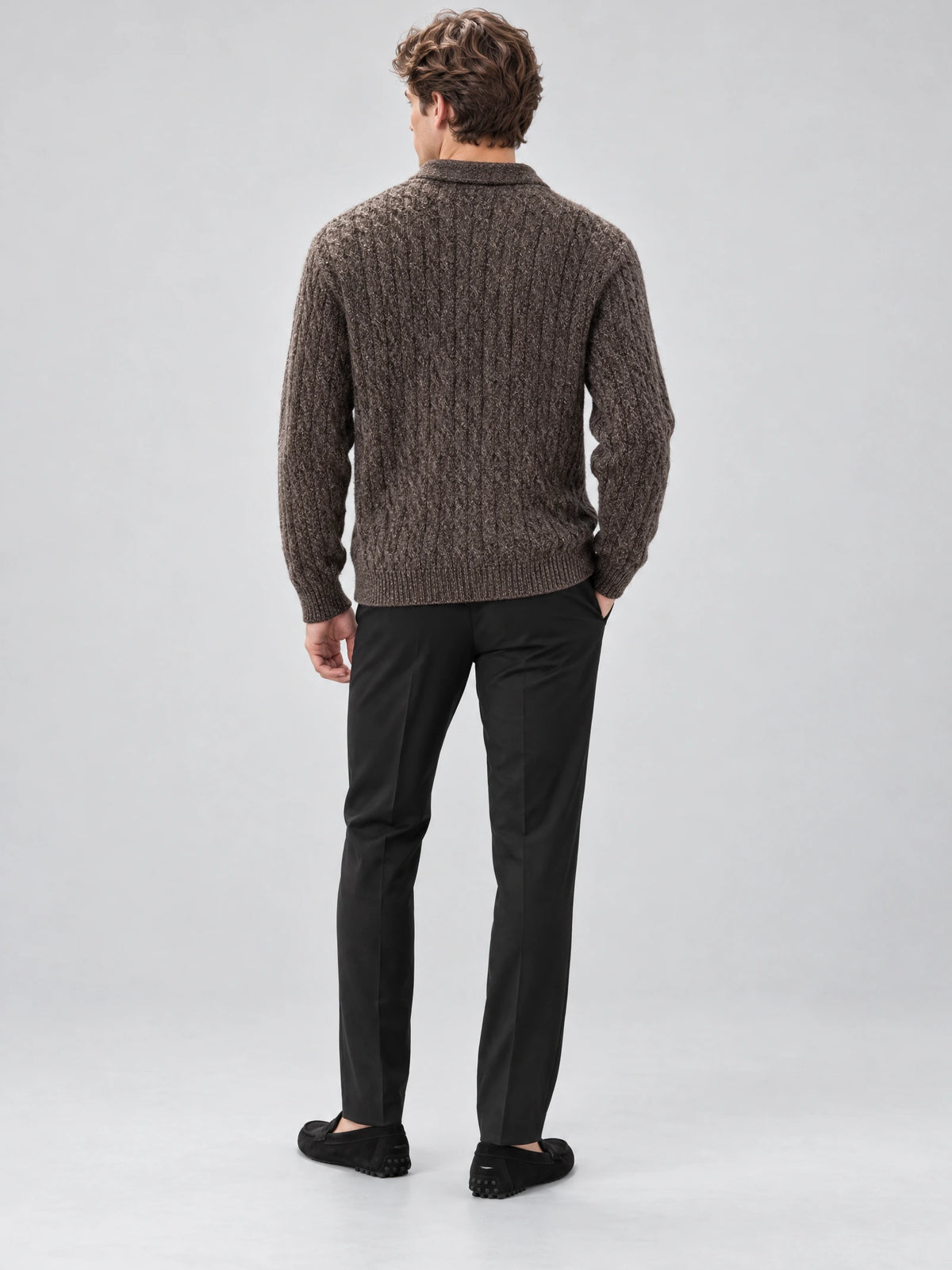 Rear studio view of a model wearing a Brown cable knit pullover with ribbed cuffs and hem.