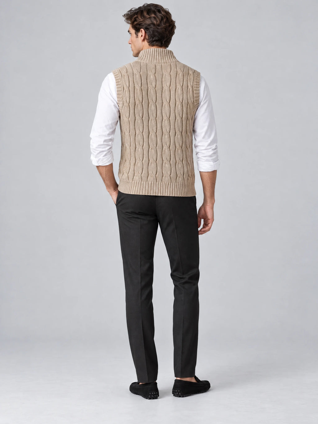 Back view of a model wearing a Khaki wool cable knit sweater vest with ribbed collar, armholes, and hem.