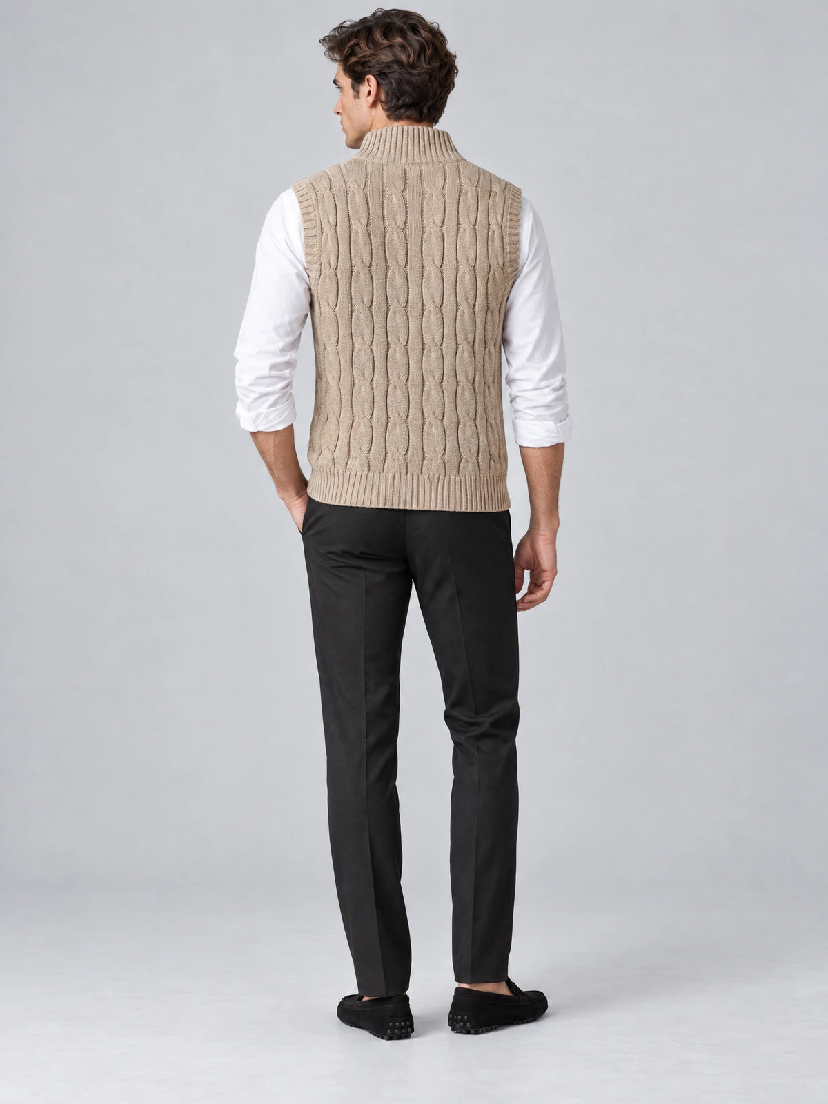 Back view of a model wearing a Khaki wool cable knit sweater vest with ribbed collar, armholes, and hem.