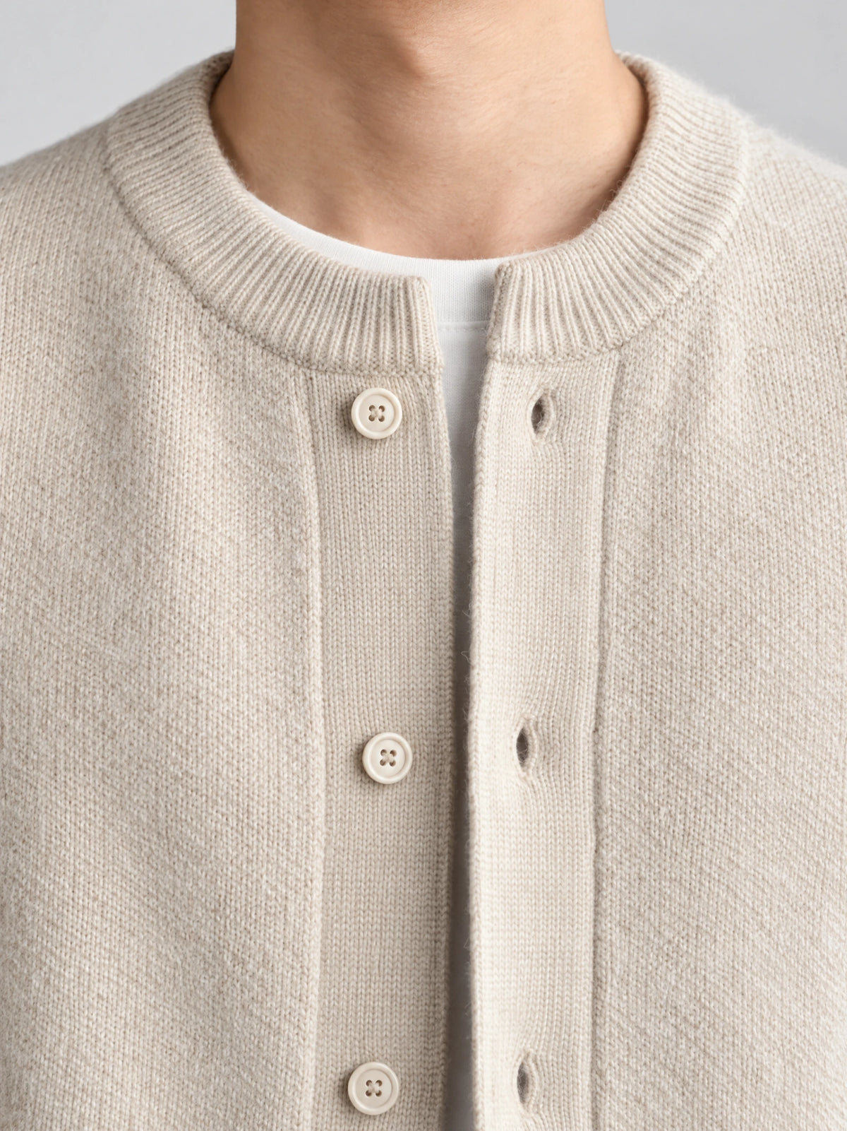 Close-up of a Beige wool Cardigan Sweater with a ribbed round neckline and button-front knit detail.