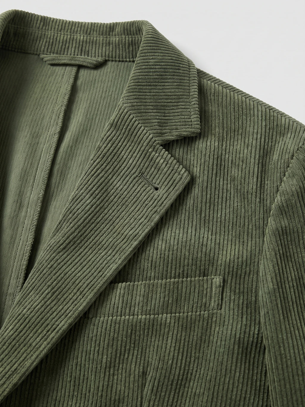 Close-up of the Green Corduroy Blazer showing the ribbed fabric, notched lapel, chest welt pocket, and inner lining.