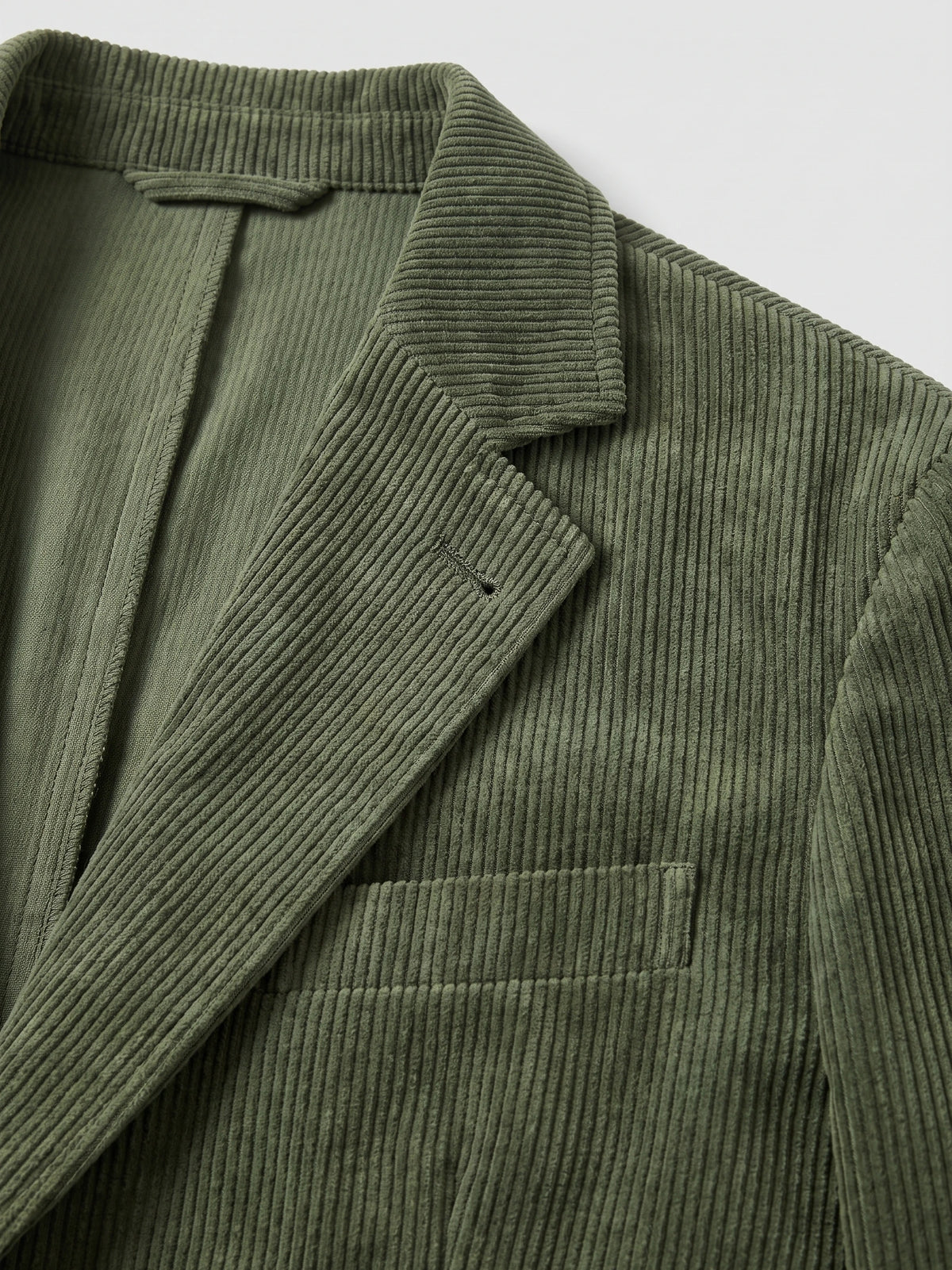 Close-up of the Green Corduroy Blazer showing the ribbed fabric, notched lapel, chest welt pocket, and inner lining.
