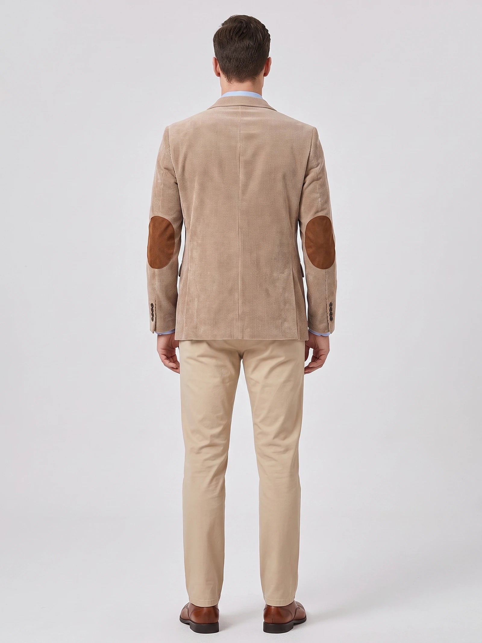 Rear studio view of a model wearing a Khaki corduroy blazer with elbow patches and a center back seam.