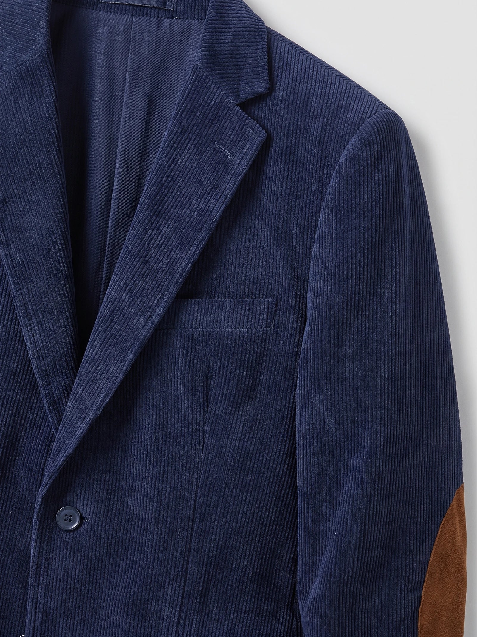 Close-up of a Navy corduroy blazer showing the notched lapel, chest welt pocket, button closure, and elbow patch.