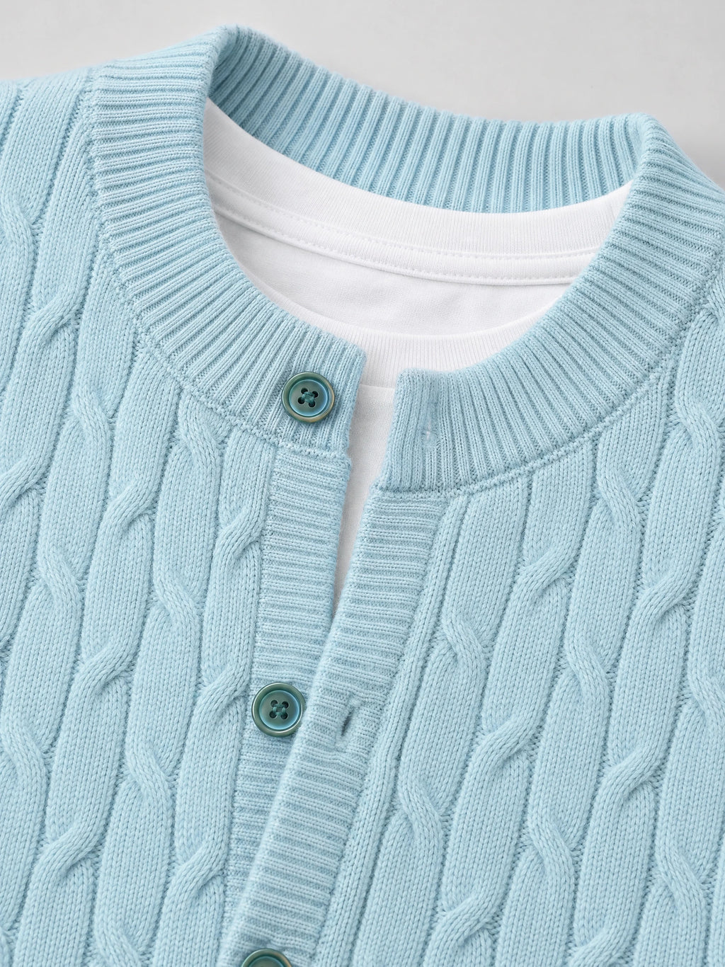 Close-up of a Blue crewneck cardigan with cable-knit texture, ribbed trim, and button-front placket.
