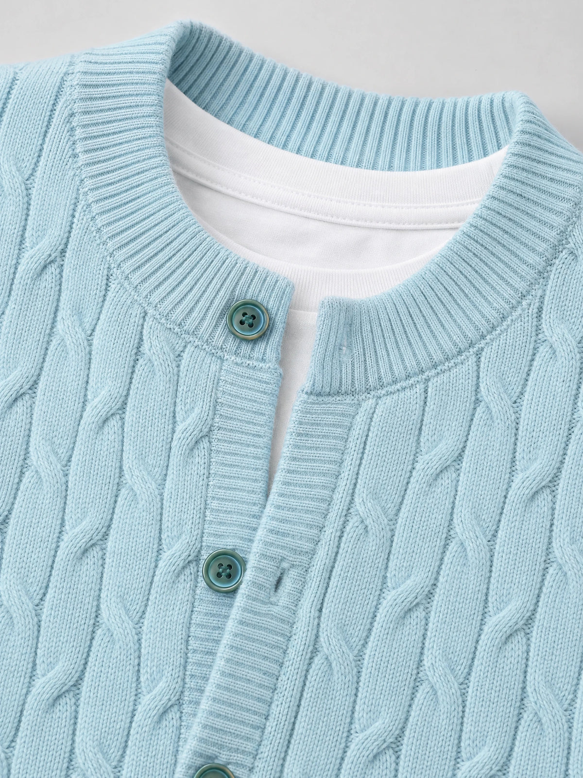 Close-up of a Blue crewneck cardigan with cable-knit texture, ribbed trim, and button-front placket.