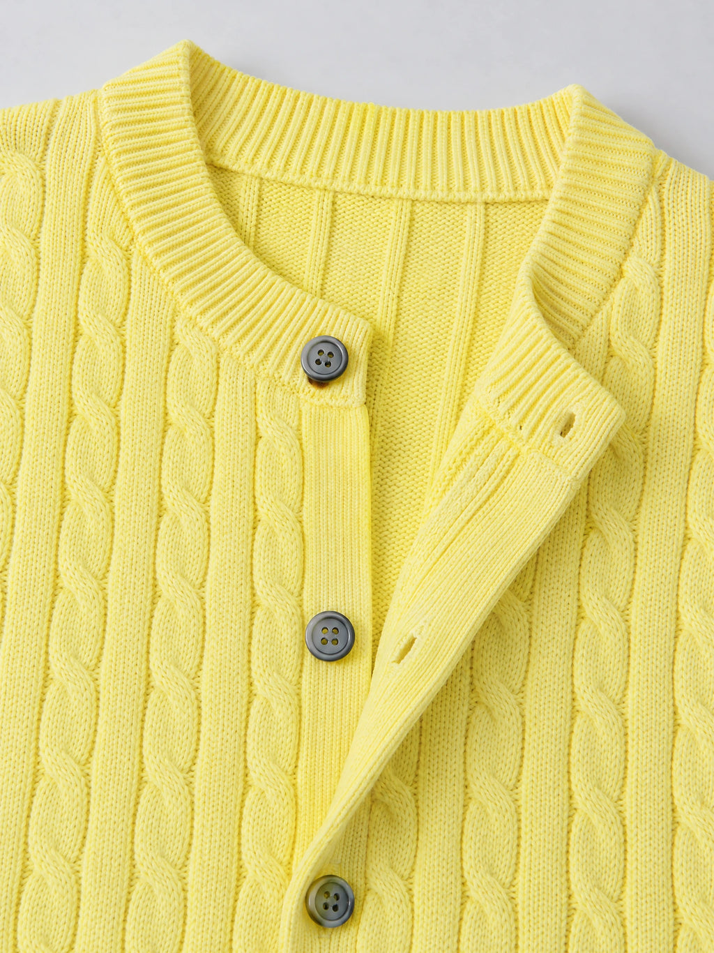 Close-up of the Yellow crewneck cardigan showing cable-knit texture, ribbed collar and button placket.
