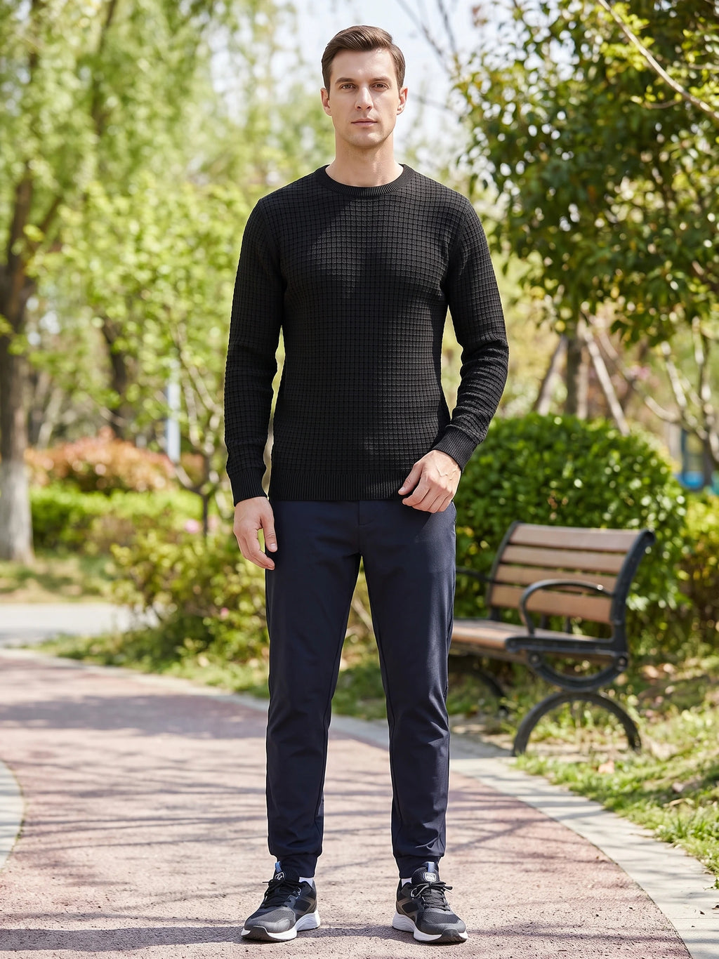 Man wearing a Black Men's Crewneck Sweater with textured knit pattern while standing on a tree-lined park path.