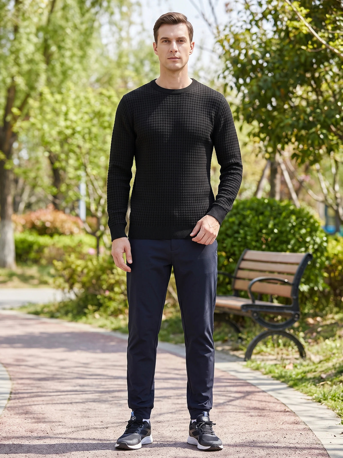 Man wearing a Black Men's Crewneck Sweater with textured knit pattern while standing on a tree-lined park path.