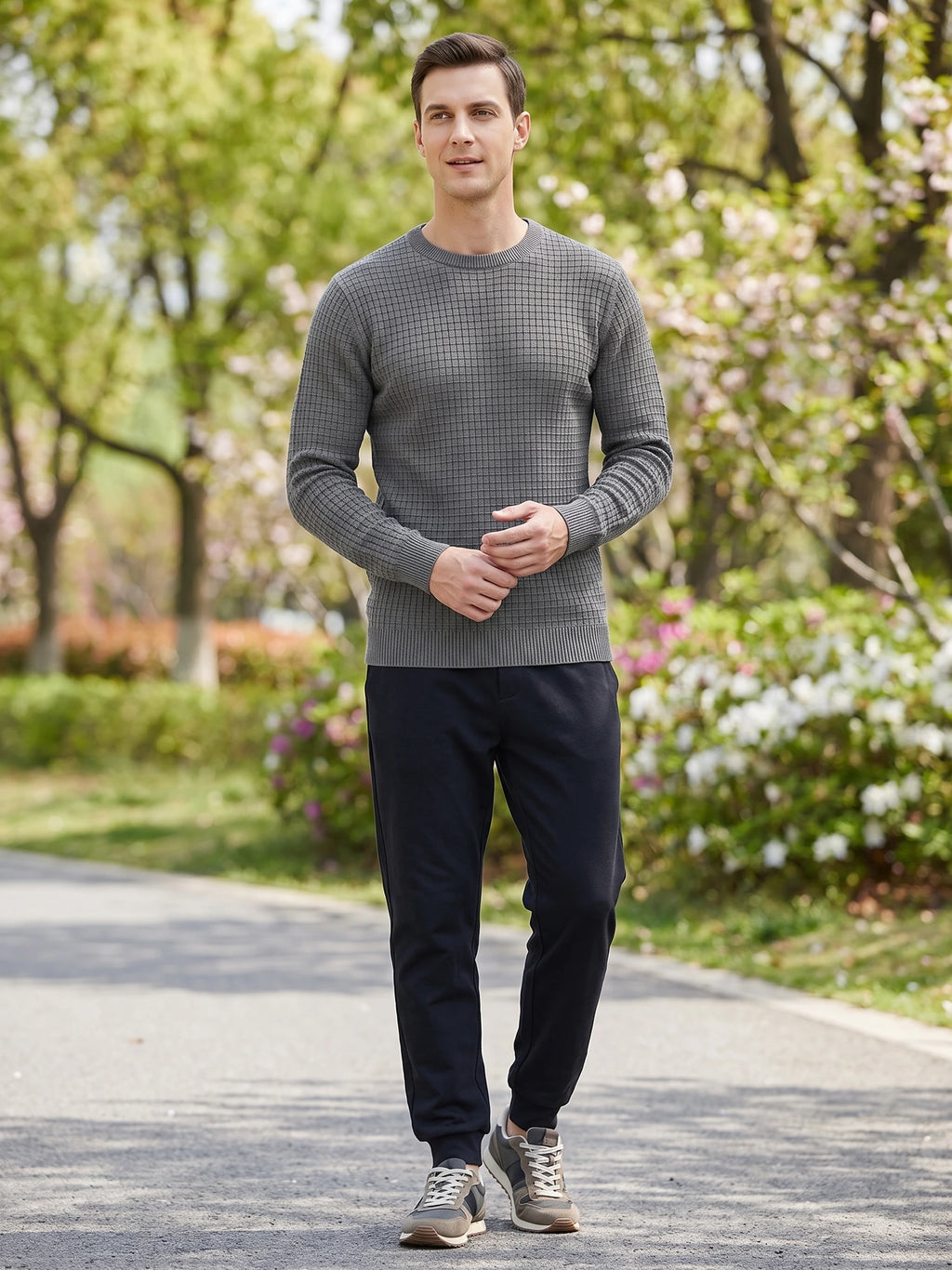 Model wearing a Gray men's crewneck sweater with a textured knit pattern while walking along a garden path.