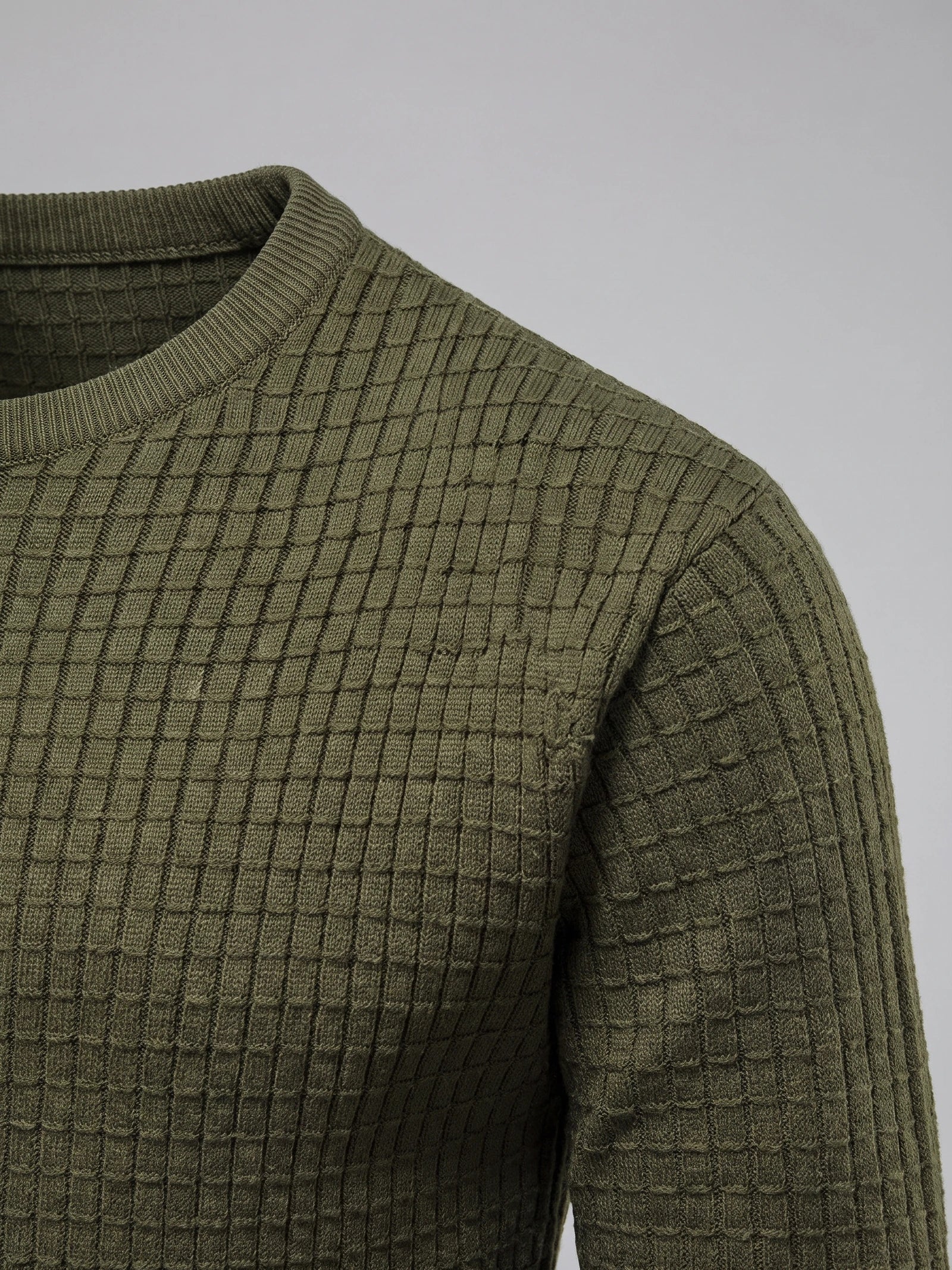 Green men's crewneck sweater detail showing a ribbed collar and textured grid-knit shoulder and sleeve.