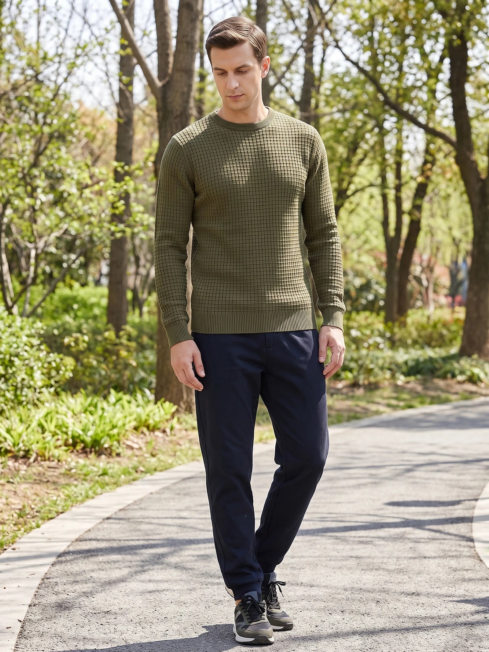 Man wearing a Green men's crewneck sweater with textured knit pattern while walking on a tree-lined path.