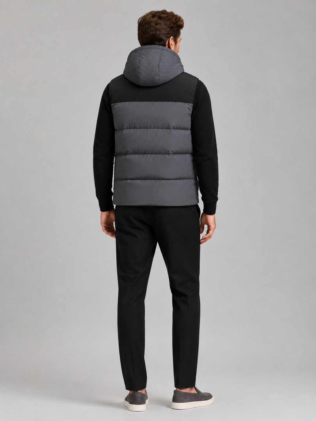 Back view of a man wearing a dark gray hooded puffer vest showing the attached hood, padded construction, sleeveless cut, and comfortable fit