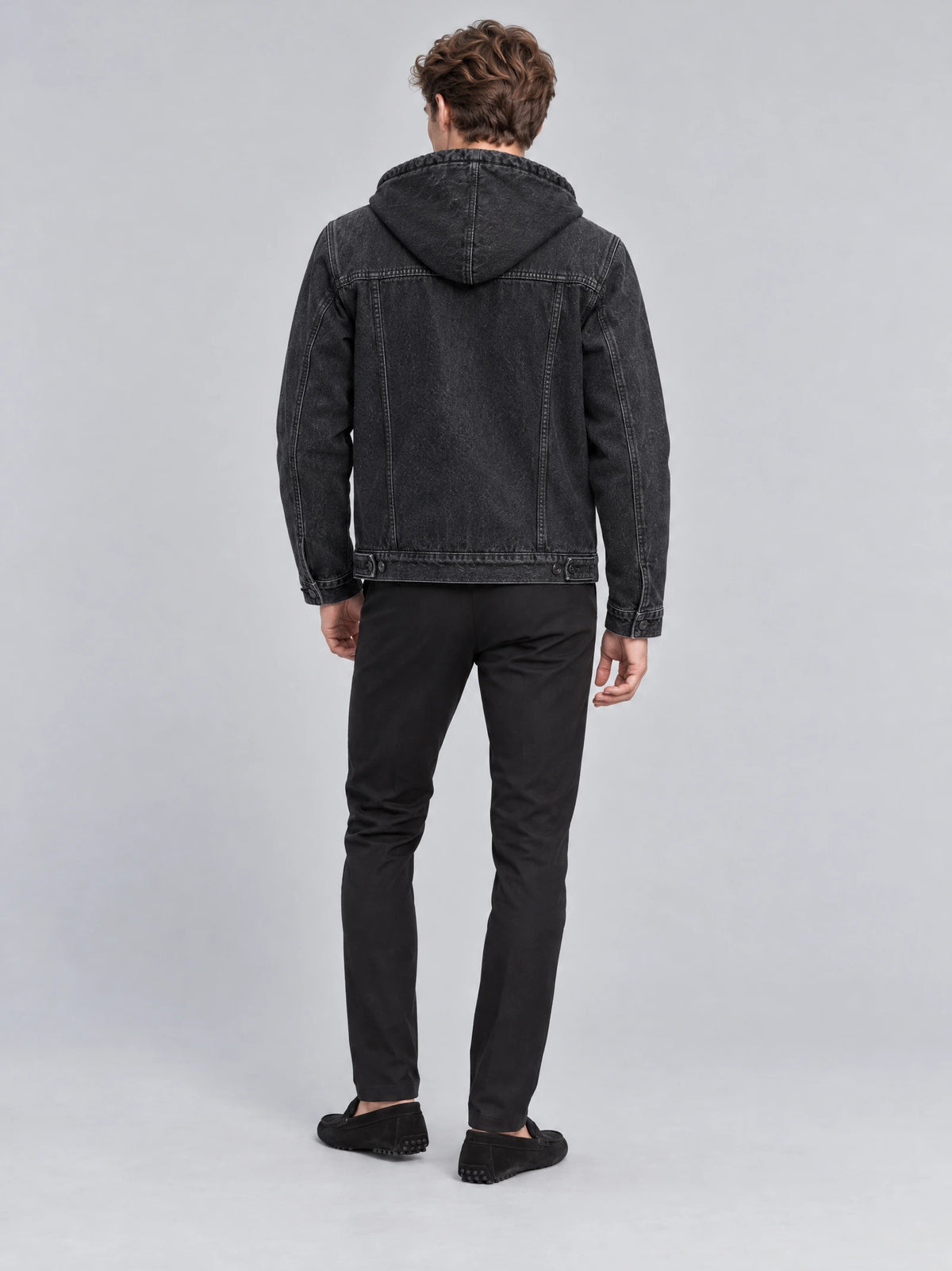 Rear studio view of a model wearing a Black mens denim hoodie jacket with a hood, back yoke stitching, and adjustable hem tabs.