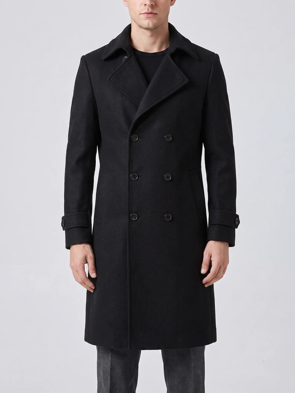 Front studio view of a model wearing a Black double-breasted trench coat with a turn-down collar and cuff tabs.