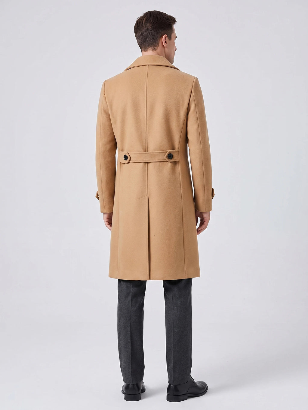 Rear studio view of a model wearing a Khaki men’s trench coat with a back vent and buttoned waist tab.