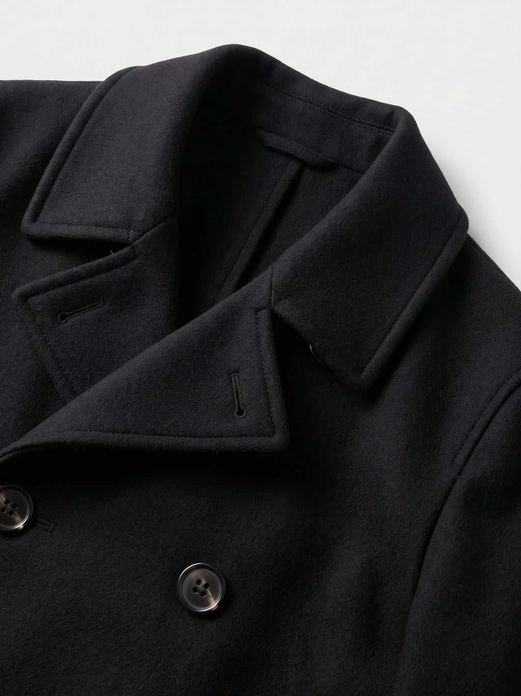 Close-up of the Black wool Peacoat showing its wide notched lapels, stitched edges, buttonholes, and double-breasted buttons.
