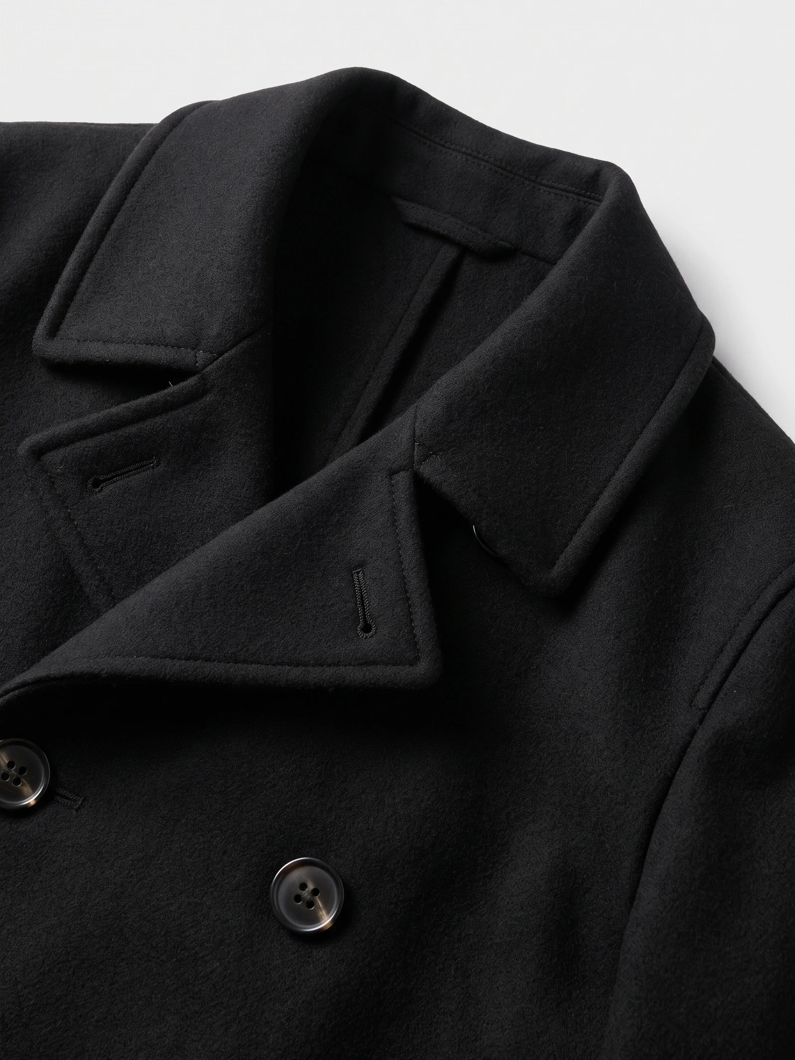 Close-up of the Black wool Peacoat showing its wide notched lapels, stitched edges, buttonholes, and double-breasted buttons.