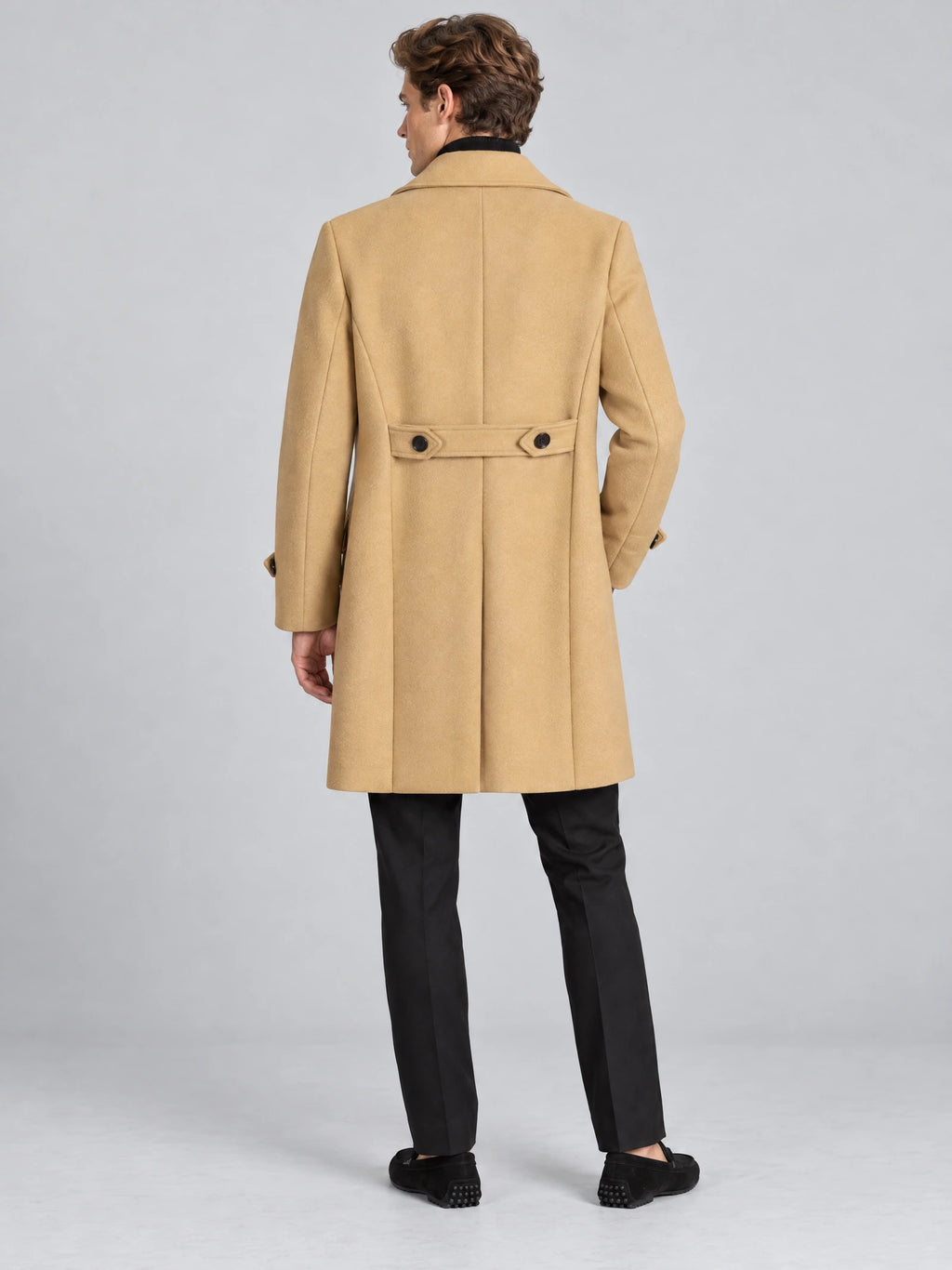 Rear studio view of a model wearing a Khaki double-breasted woolen coat with a buttoned back belt and center back vent.