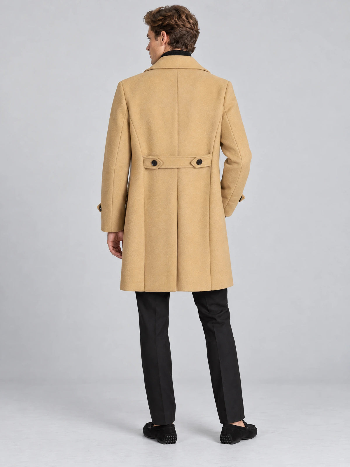 Rear studio view of a model wearing a Khaki double-breasted woolen coat with a buttoned back belt and center back vent.