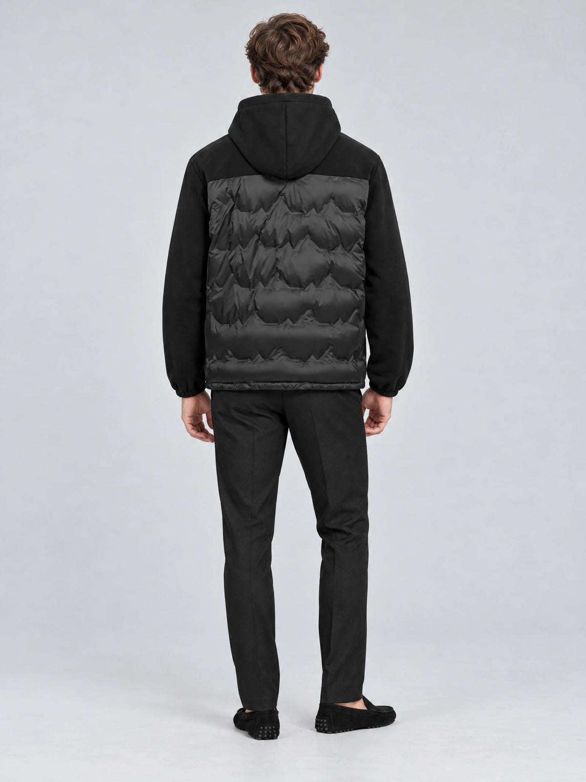 Rear studio view of a model wearing a Black hooded Down Jacket with a quilted back panel and long sleeves.