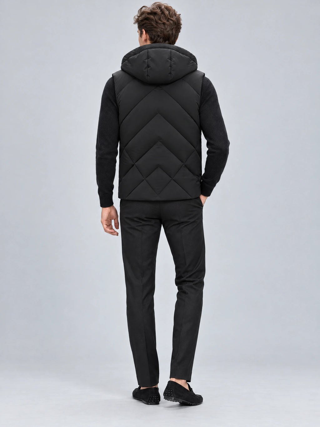 Rear studio view of a model wearing a Black Down Vest with a hood and geometric quilted back panels.