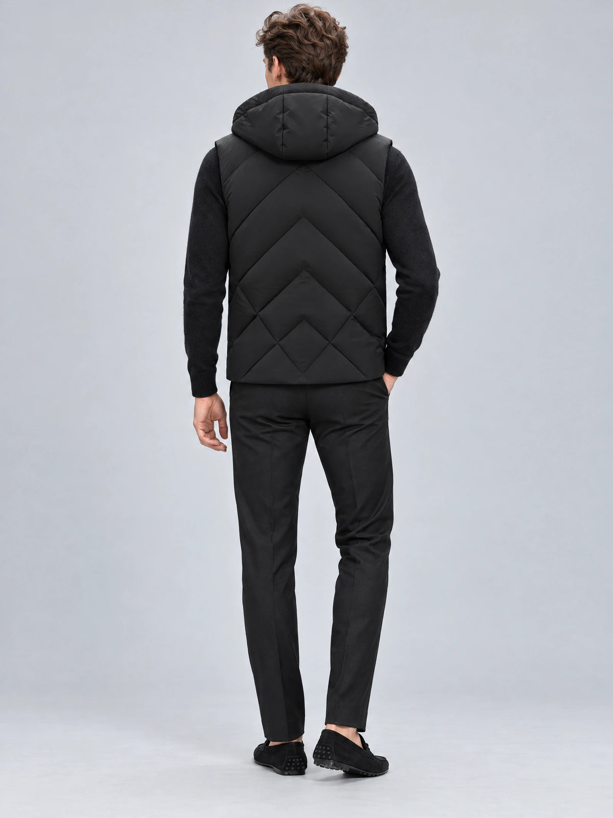 Rear studio view of a model wearing a Black Down Vest with a hood and geometric quilted back panels.