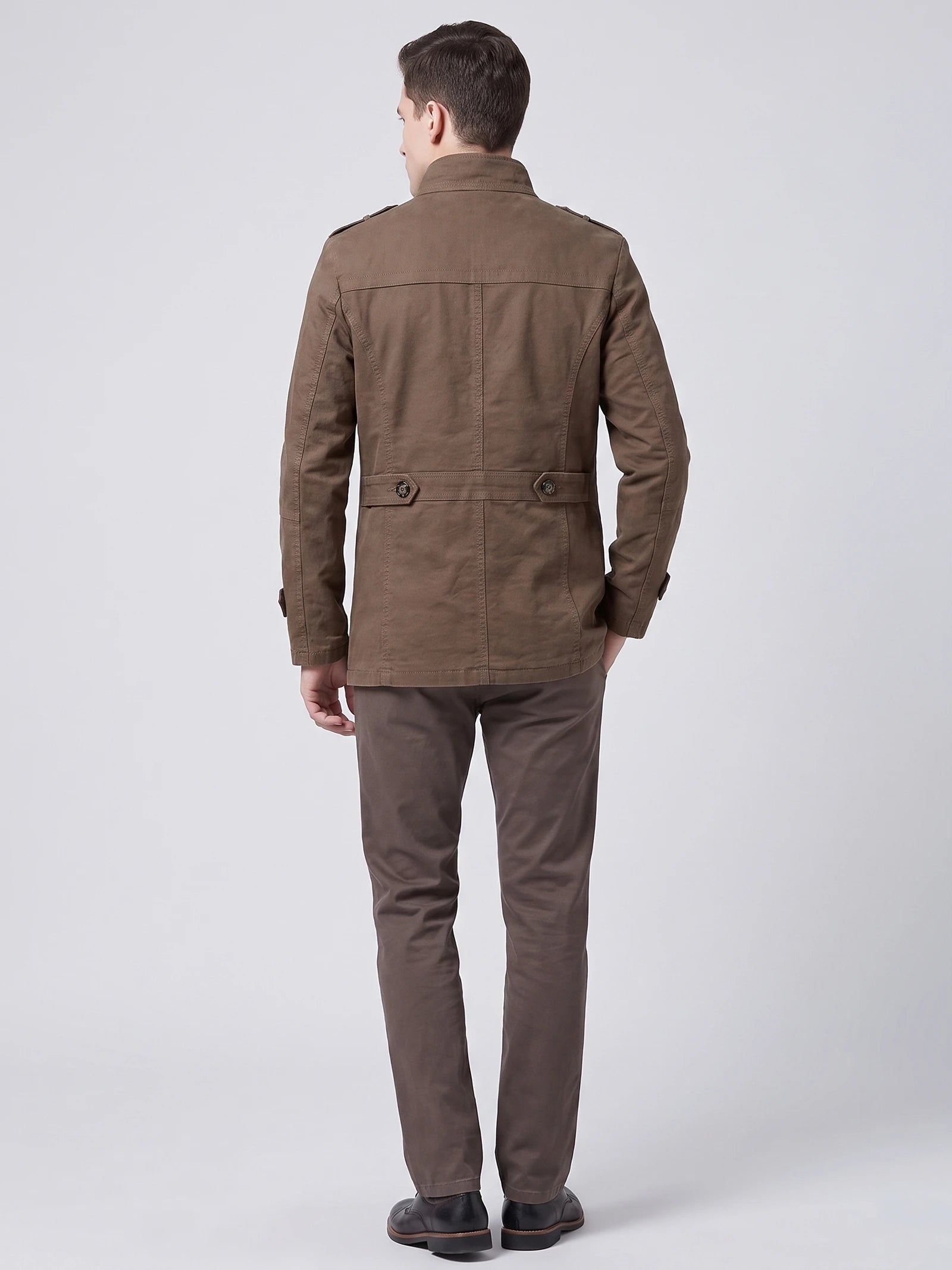 Rear studio view of a model wearing a Brown cotton Fall Trench Coat with a back waist tab and stitched paneling.