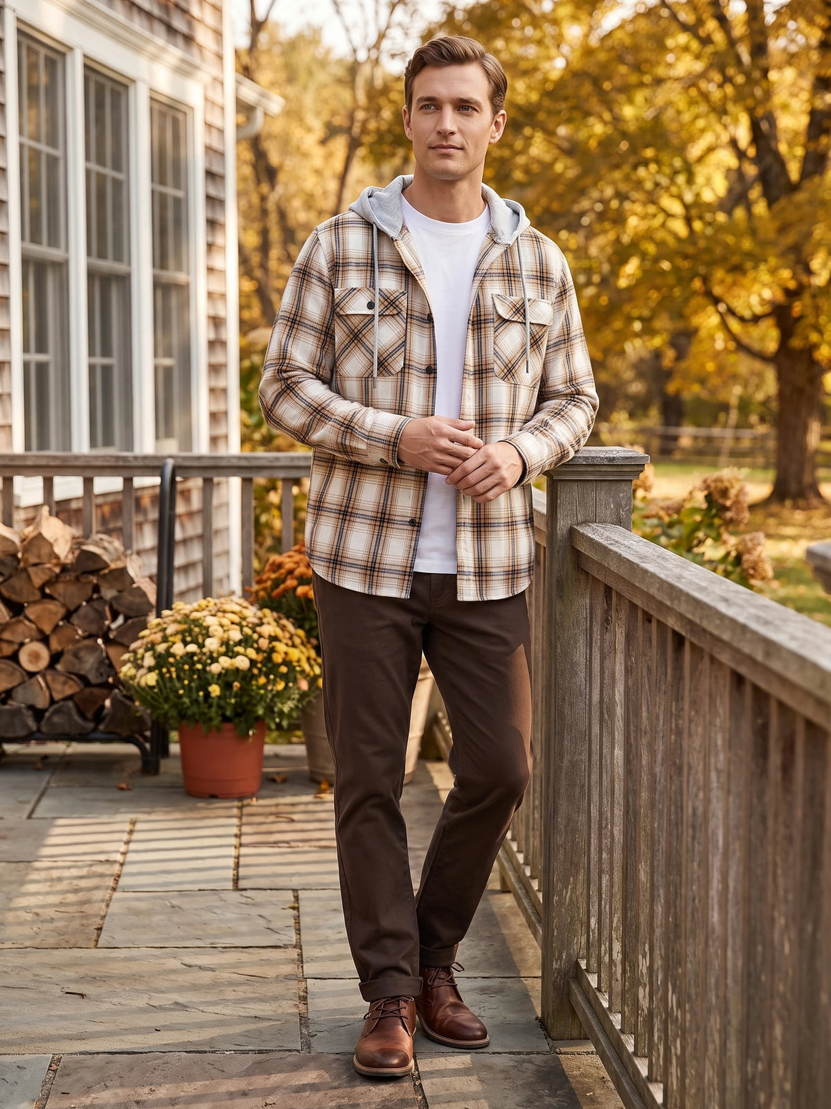 Man wearing a Yellow hooded plaid Flannel Jacket with chest pockets while standing on a porch beside autumn trees.