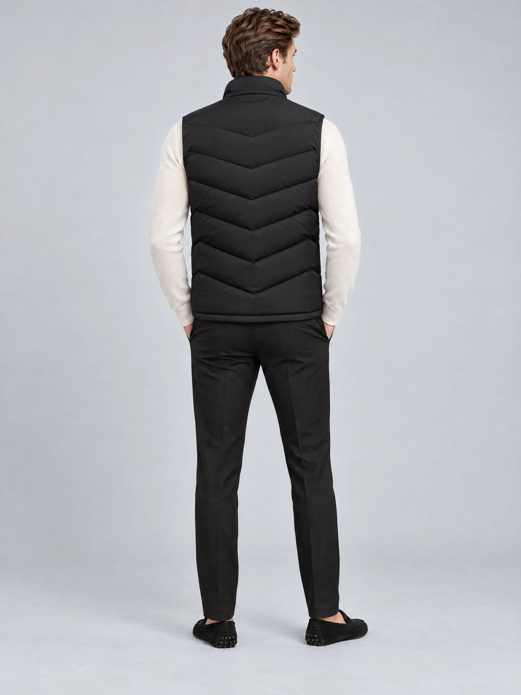 Rear studio view of a model wearing a Black fleece lined puffer vest with a stand collar and chevron quilted back.