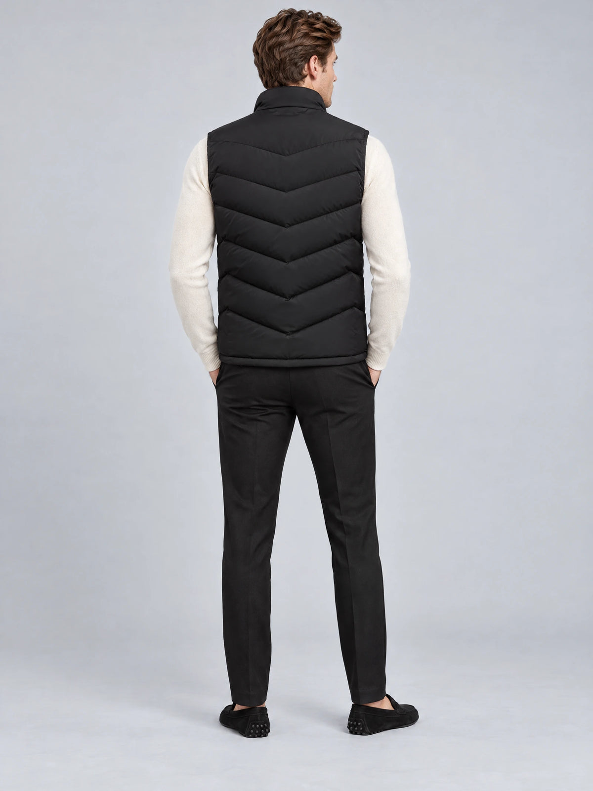 Rear studio view of a model wearing a Black fleece lined puffer vest with a stand collar and chevron quilted back.