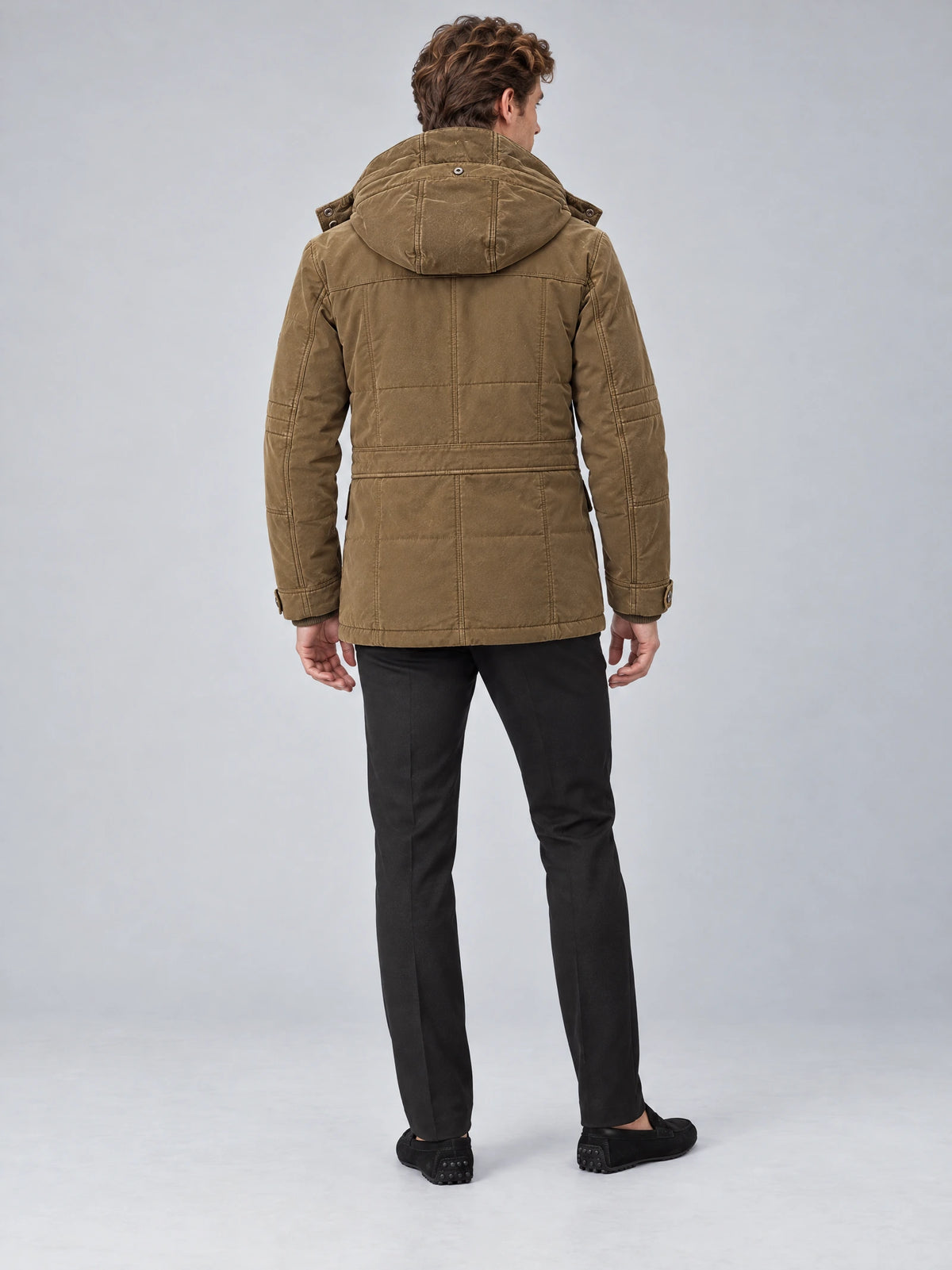 Rear studio view of a model wearing a Brown heavy winter jacket with a hood, paneled back stitching, and adjustable cuffs.