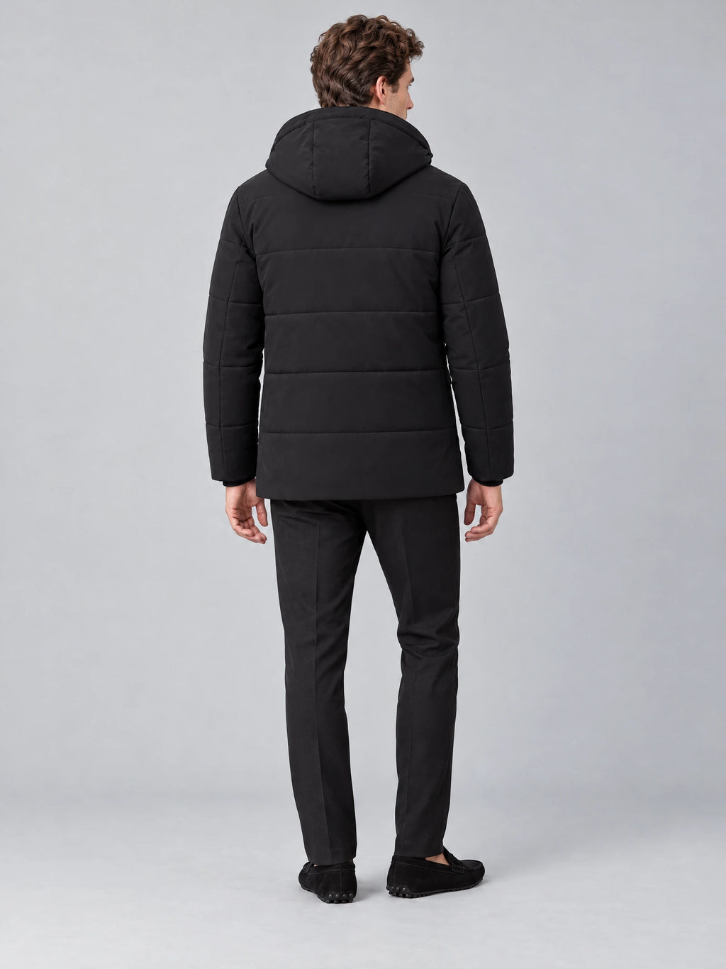 Rear studio view of a model wearing a Black Heavy Winter Jacket with a padded hood and horizontal quilted back panels.