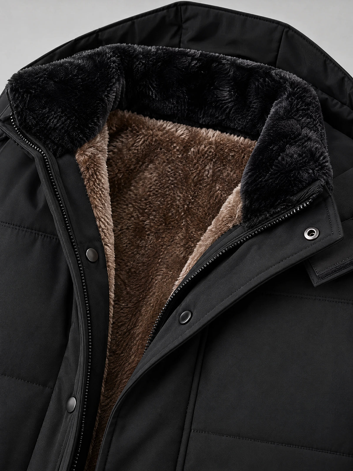 Black heavy winter jacket close-up showing the plush fleece-lined stand collar, zipper, and snap-button storm flap.