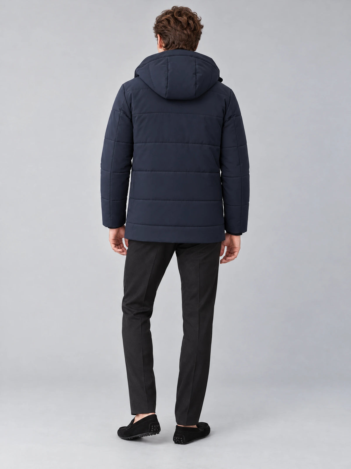 Rear studio view of a model wearing a Navy Heavy Winter Jacket with a padded hood and horizontal quilted panels.