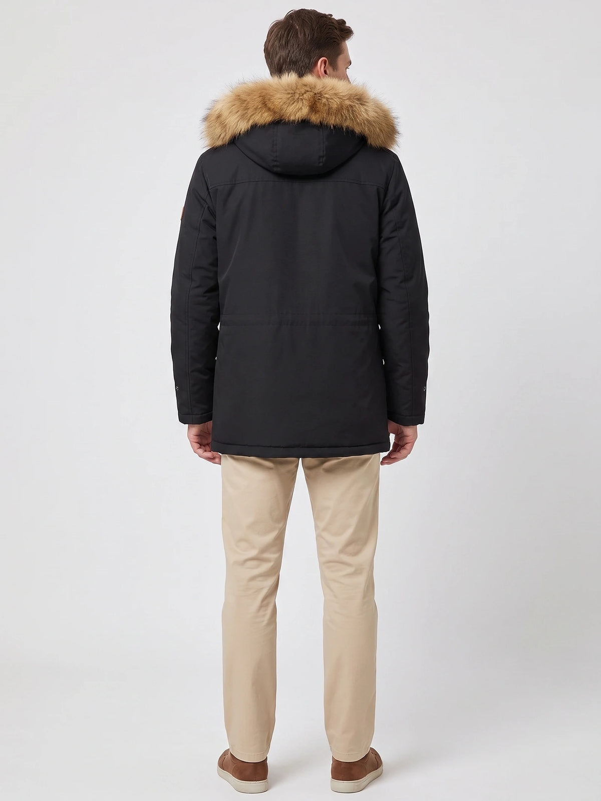 Rear studio view of a model wearing a Black men's parka with a fur-trimmed hood and quilted back seams.