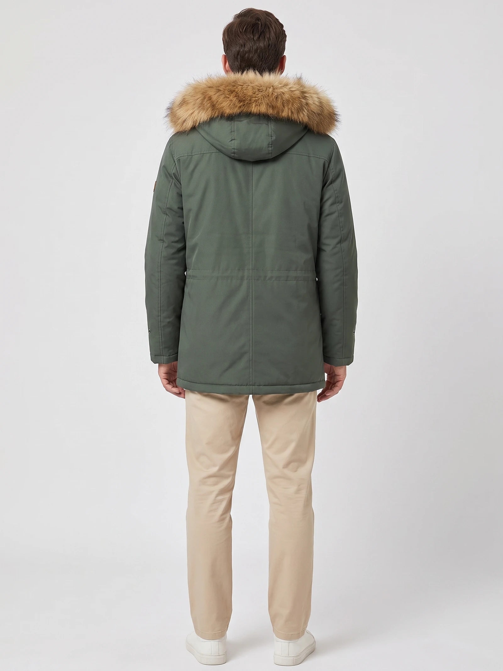 Rear studio view of a model wearing a Green men's parka with a fur-trimmed hood and back seam detailing.