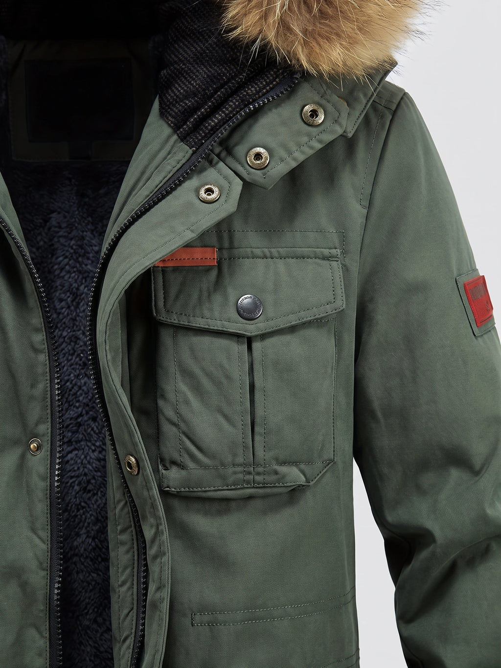 Green men's Parkas close-up showing the zip front, snap-button storm flap, fleece-lined collar, and flap chest pocket.