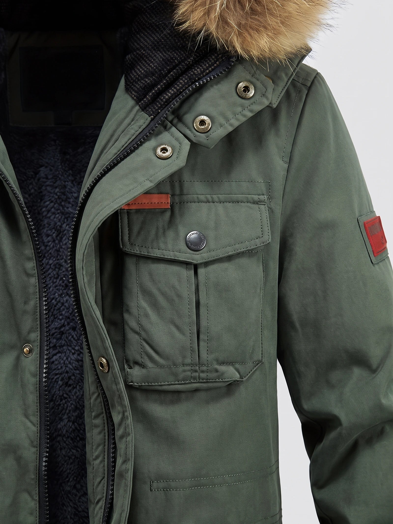 Green men's Parkas close-up showing the zip front, snap-button storm flap, fleece-lined collar, and flap chest pocket.