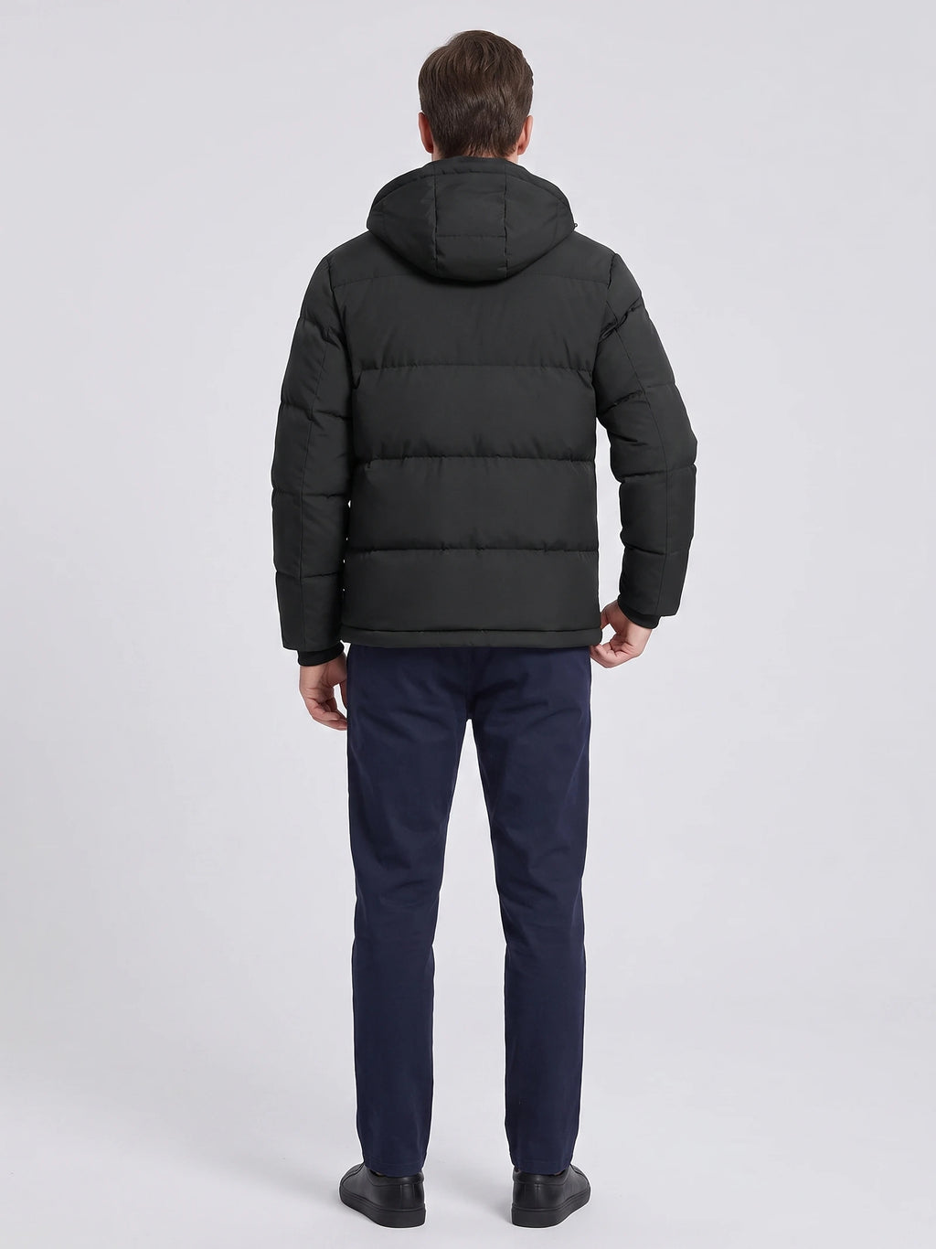 Rear view of a model wearing a Black hooded puffer jacket with horizontal quilting and a padded hood.