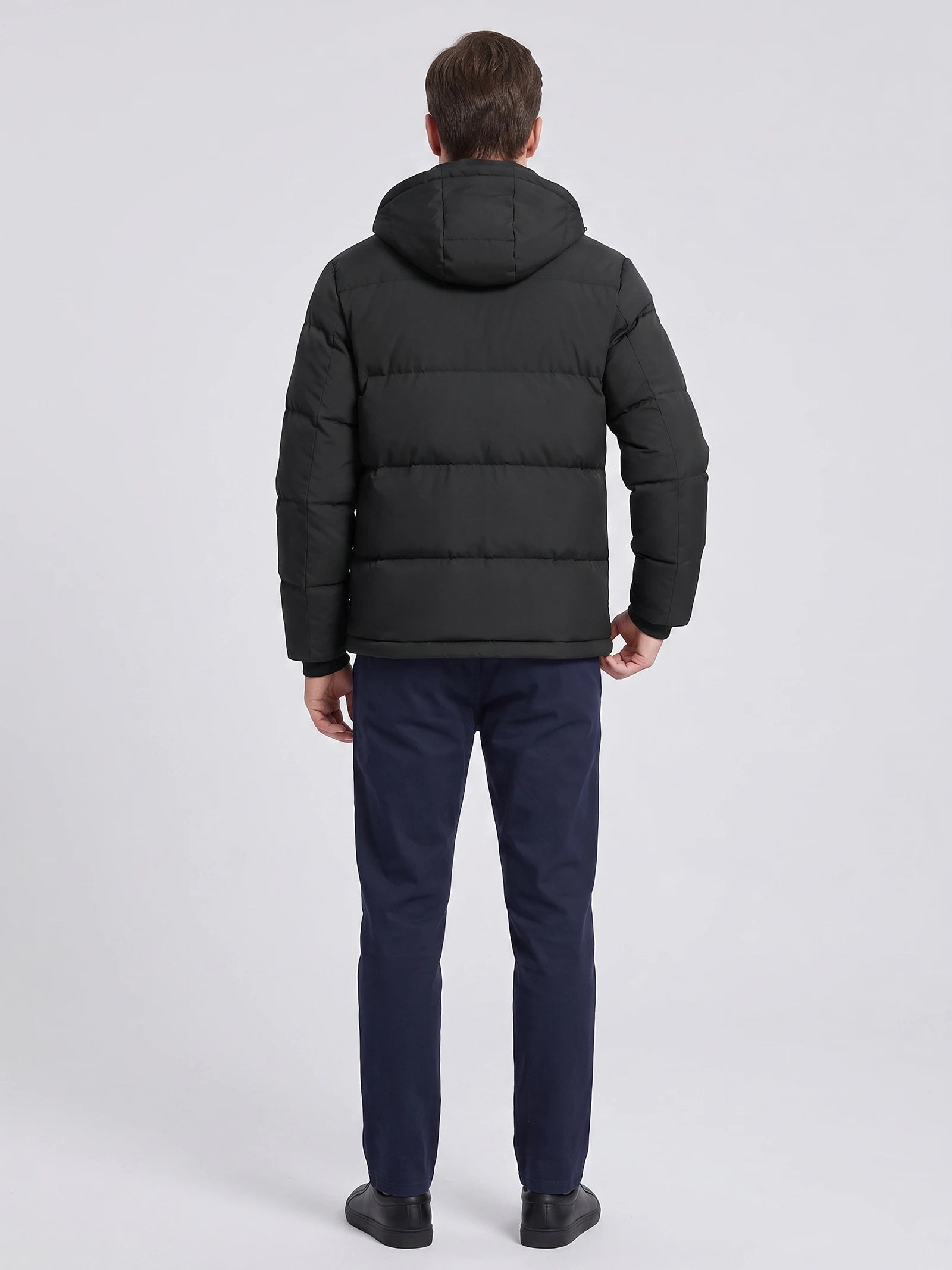 Rear view of a model wearing a Black hooded puffer jacket with horizontal quilting and a padded hood.